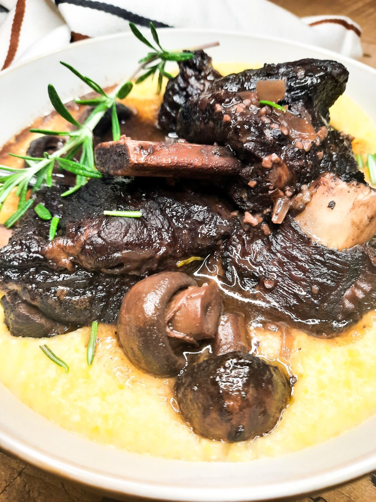 Red Wine Braised Short Ribs are first seared then cooked low and slow until fork tender with tender mushrooms and herbs in a pool of polenta.
