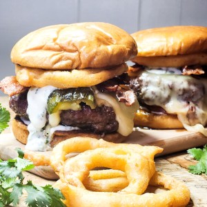 OUT WEST Roasted Jalapeno Burger piled high with bacon, onion rings, cilantro lime crema, creamy jack cheese and a buttery brioche bun.