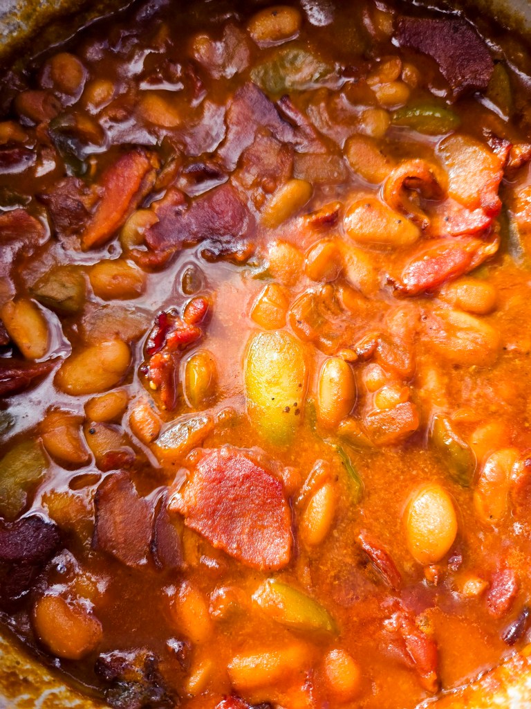 A close-up view of a rich and savory bean stew with pieces of meat, featuring various beans and vegetables simmering in a thick, flavorful broth.
